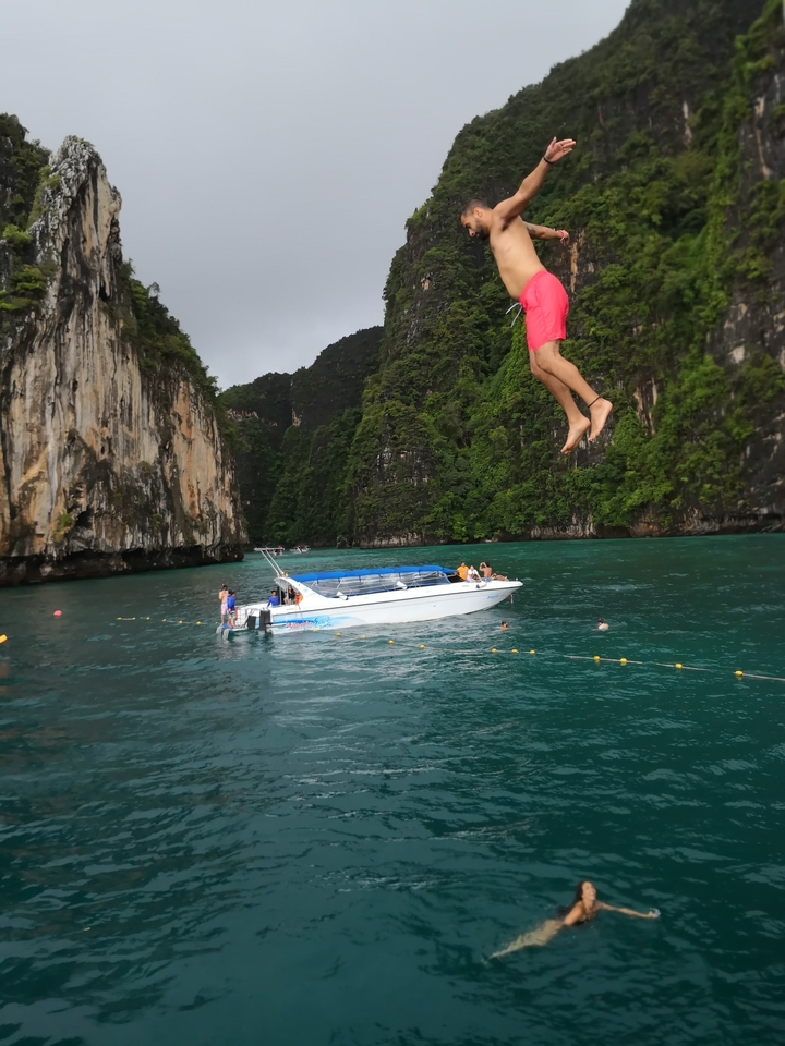Person jumping off a boat into the water with cliffs in view.