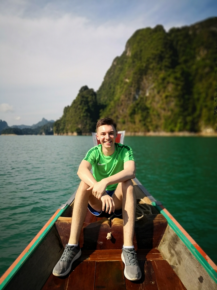 Man smiling on a boat with a mountainous backdrop.