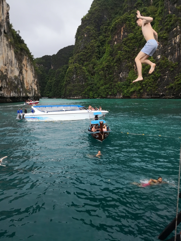 Boats and swimmers in scenic waters with cliffs.