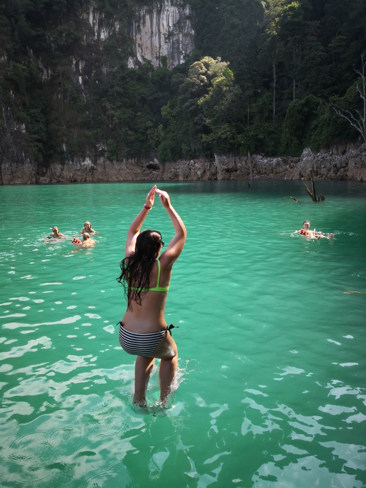 People swimming in turquoise waters in a scenic area.