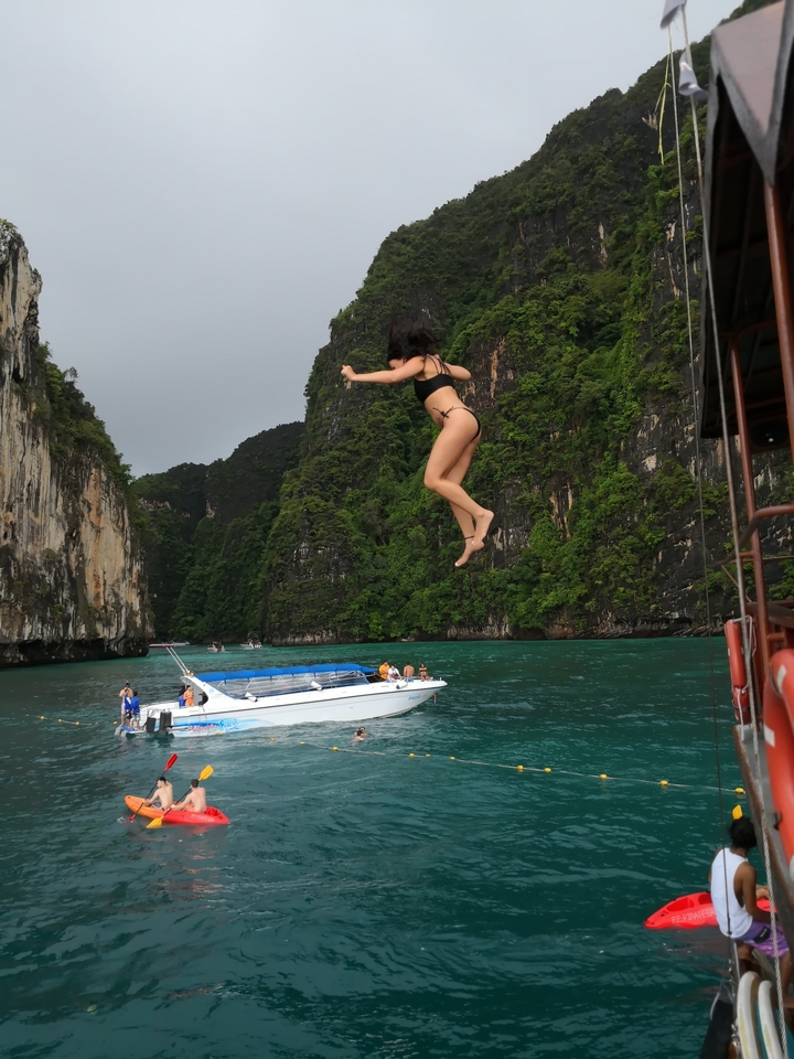 Person in mid-air jumping into water with boats nearby.