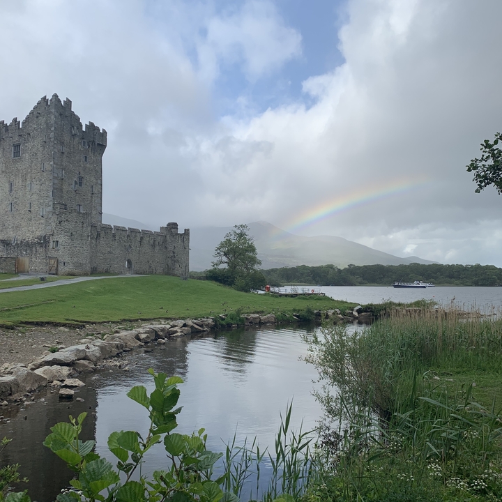 Château avec un arc-en-ciel et un lac au premier plan.