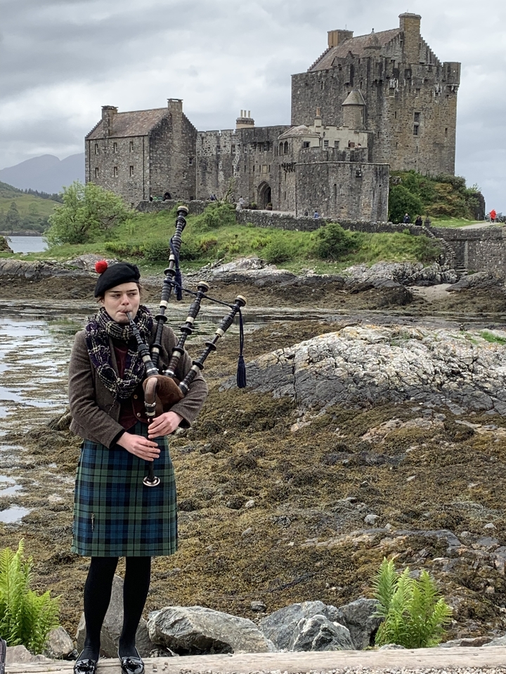 Personne en tenue traditionnelle jouant de la cornemuse sur un rivage rocheux.