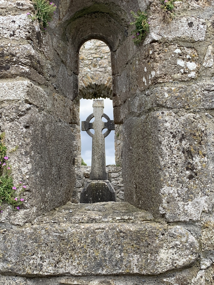 Croix en pierre encadrée par une ruine archéologique.