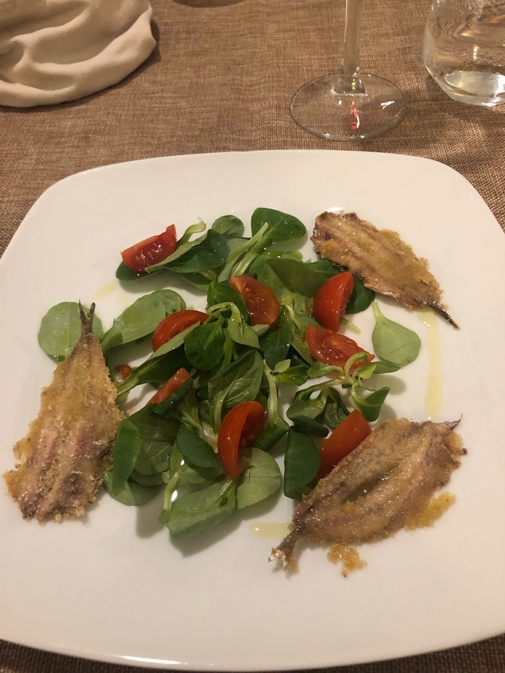 Salade avec tomates et anchois panés sur une assiette blanche.