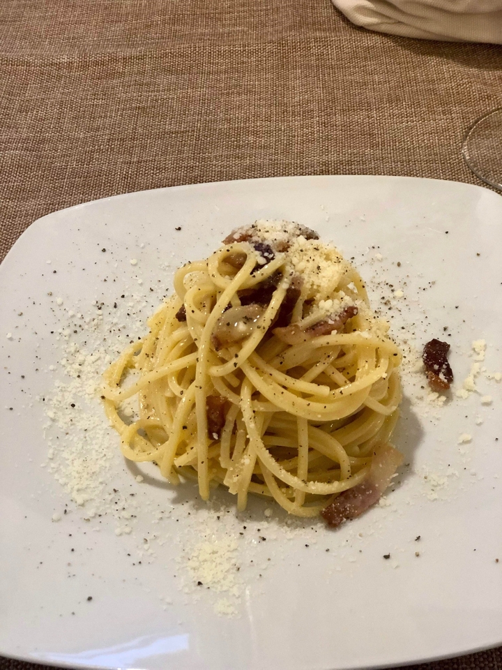 Plat de pâtes dans une assiette blanche avec du fromage et du poivre.