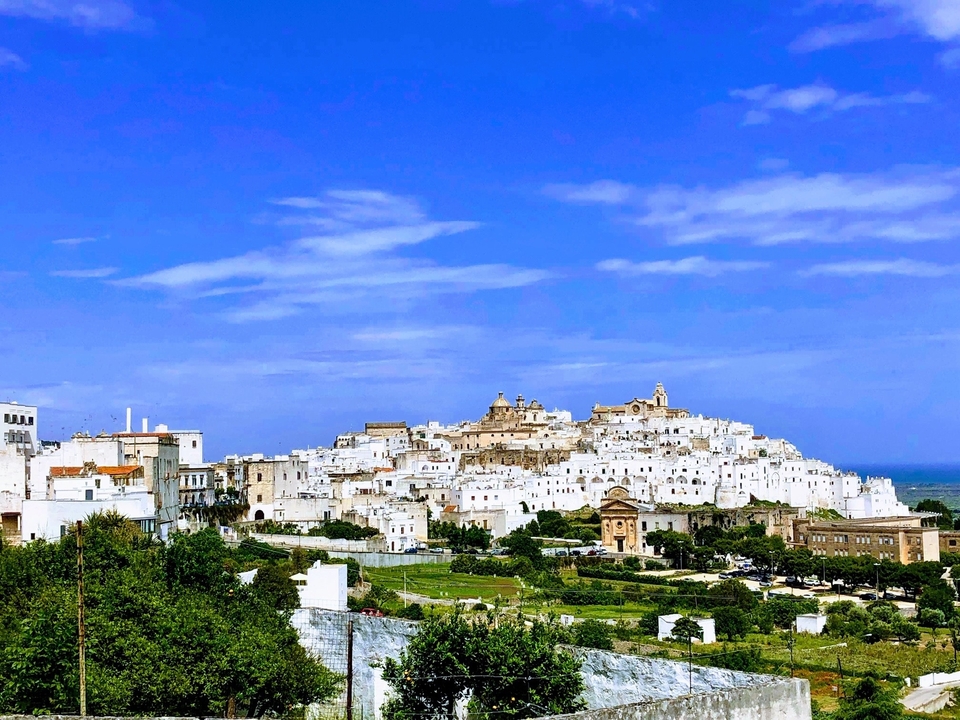 Vue panoramique d'une ville blanche perchée sur une colline sous un ciel bleu.