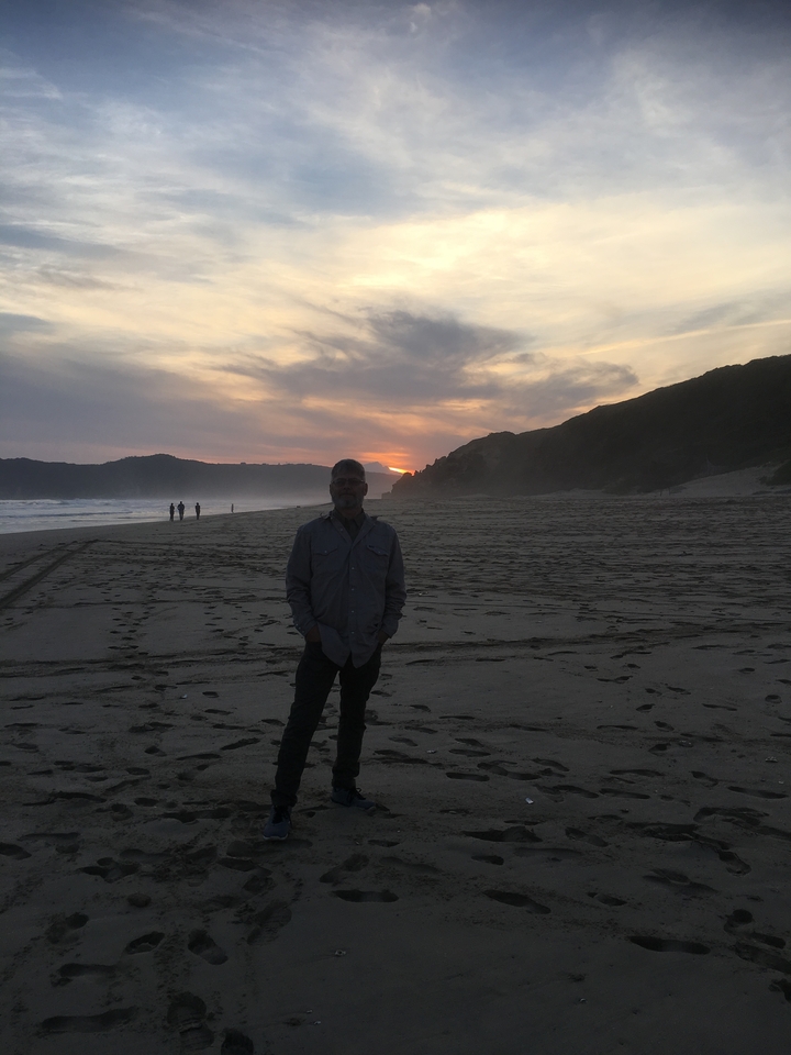 Personne debout sur une plage au coucher du soleil.