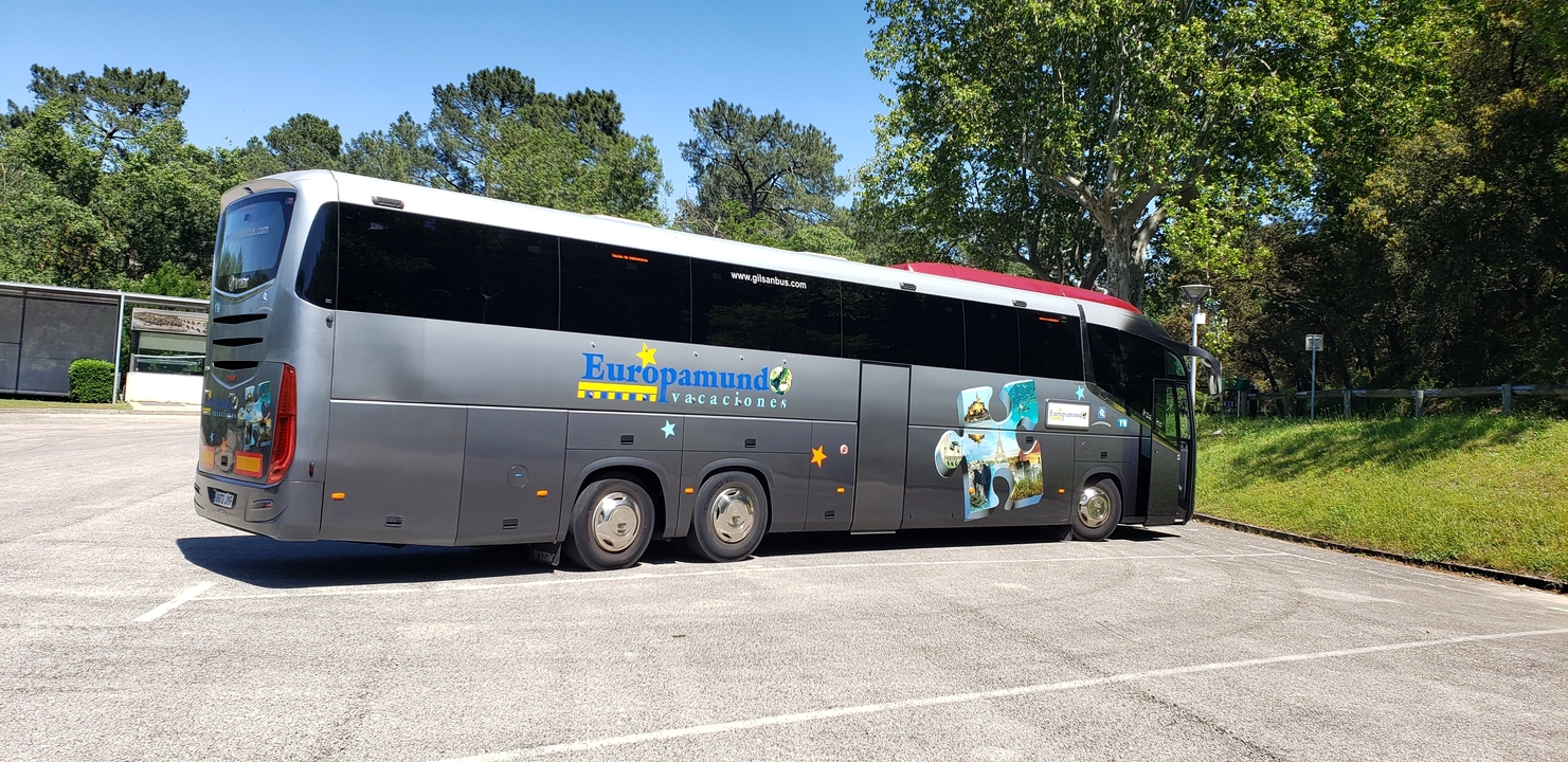 Autocar de tourisme garé dans une aire de repos bordée d'arbres.
