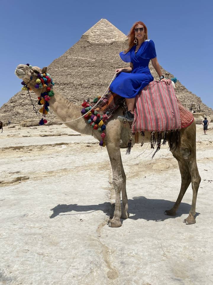 Personne sur un chameau devant une pyramide.