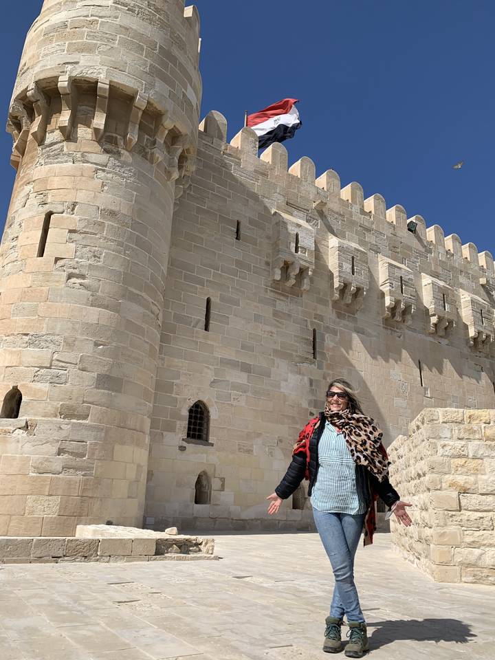 Femme posant devant un fort historique avec un drapeau.