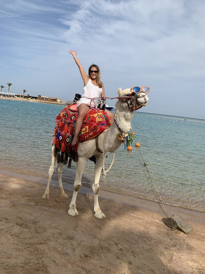 Femme montant un chameau décoré au bord de l'eau.