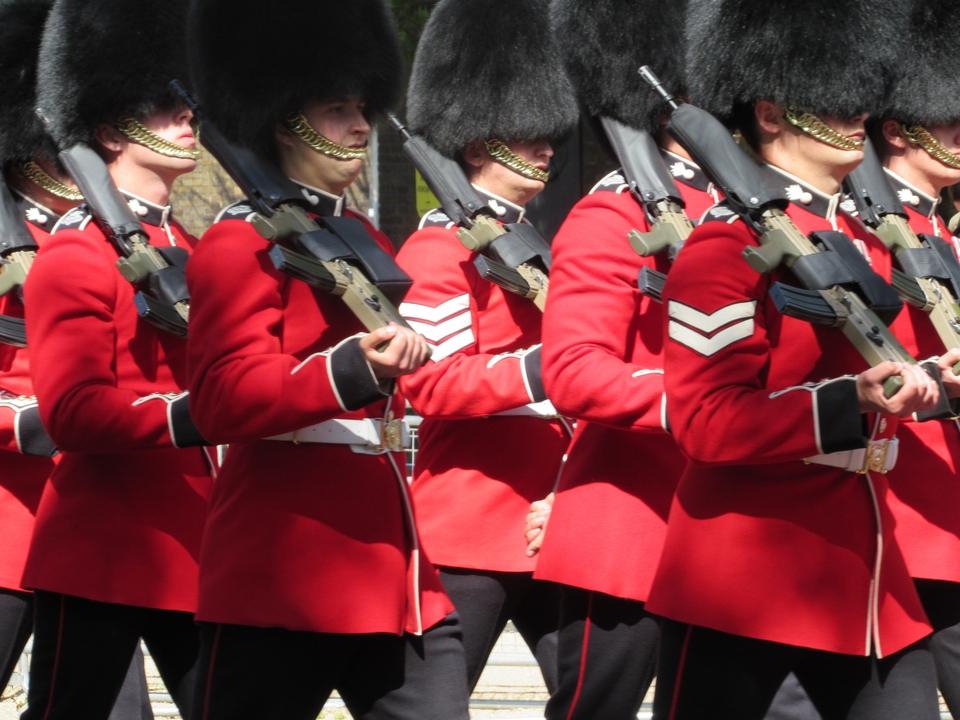 Gardes d'honneur en uniformes rouges et chapeaux en peau d'ours défilant.