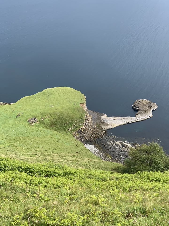 Vue aérienne d'une péninsule herbeuse et d'un rivage rocheux rejoignant la mer.