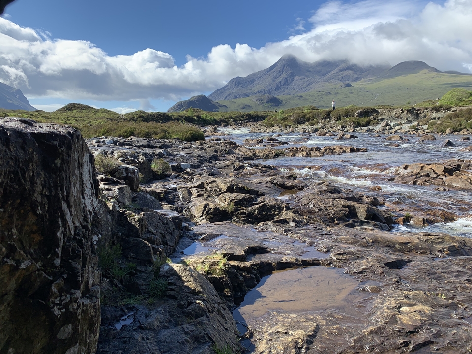 Ruisseau rocheux avec des montagnes en arrière-plan sous un ciel bleu dégagé.