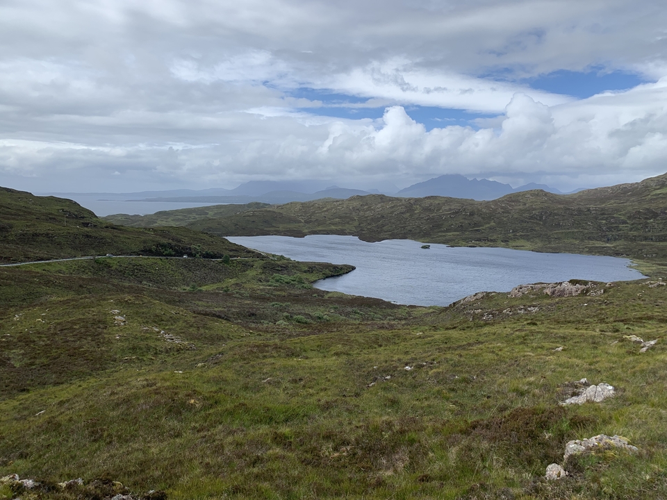 Vue panoramique d'un lac et de collines sous un ciel nuageux.