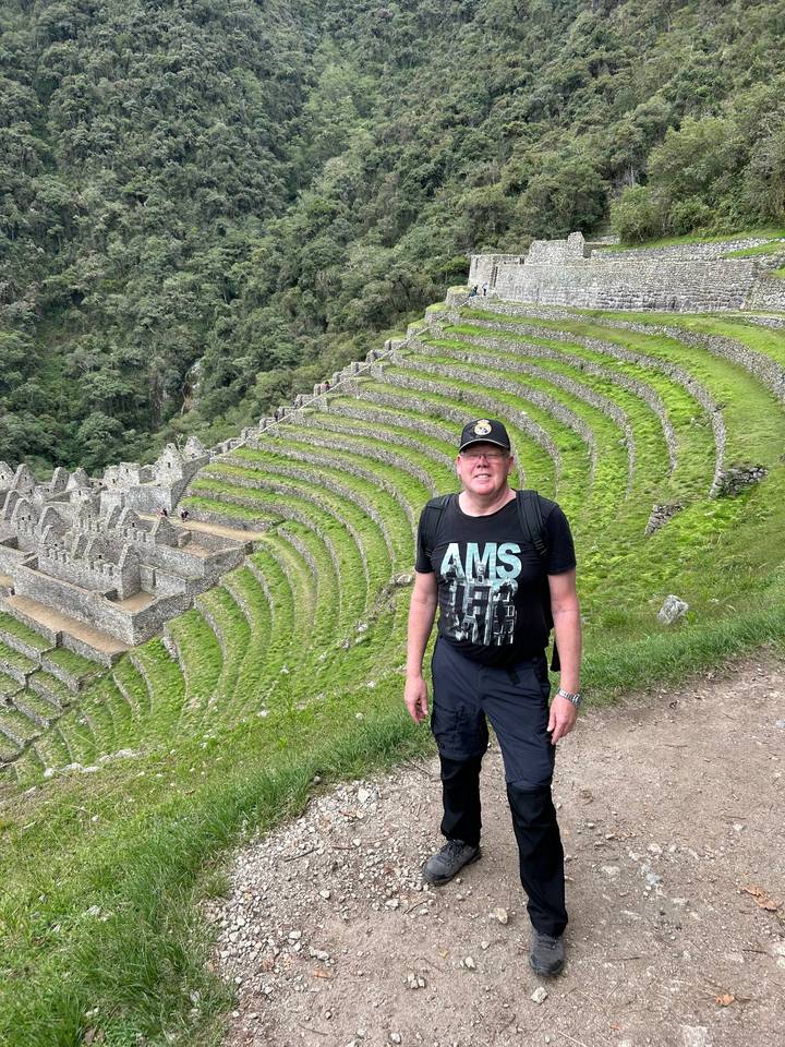 Tourist posiert vor terrassierten Hügeln und Ruinen.