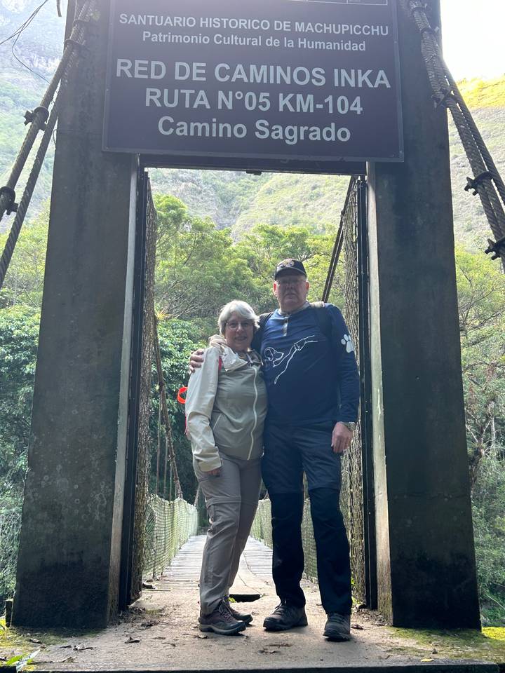 Paar steht auf einer Brücke mit Grün und Hügeln im Hintergrund.
