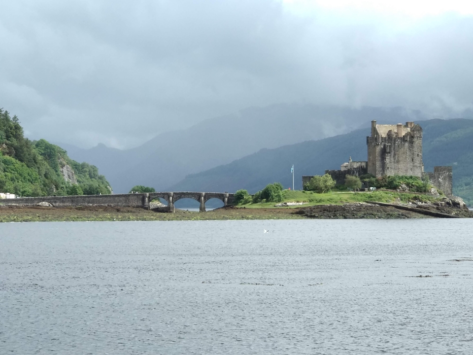 Castle beside a lake with mountains in the background.