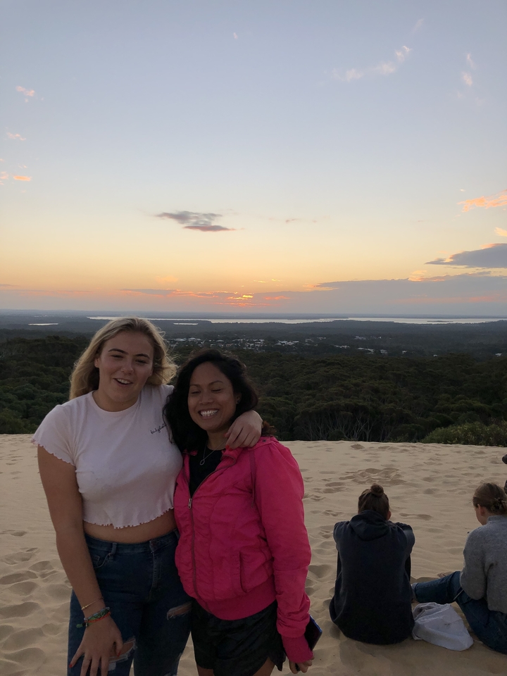 Deux personnes sur une dune de sable au coucher du soleil.