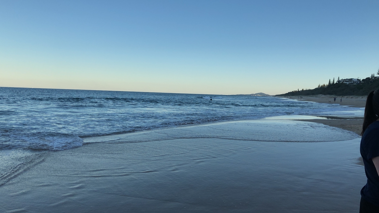 Plage avec des vagues et des collines au loin.
