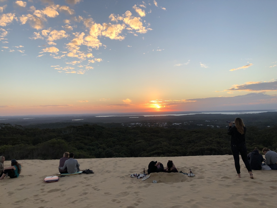 Des gens assis regardant le coucher de soleil sur une dune de sable.