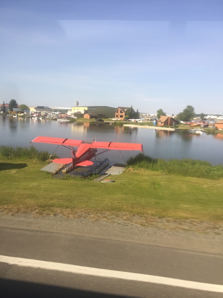 Un hydravion rouge sur un quai avec des hangars d'avions en arrière-plan.