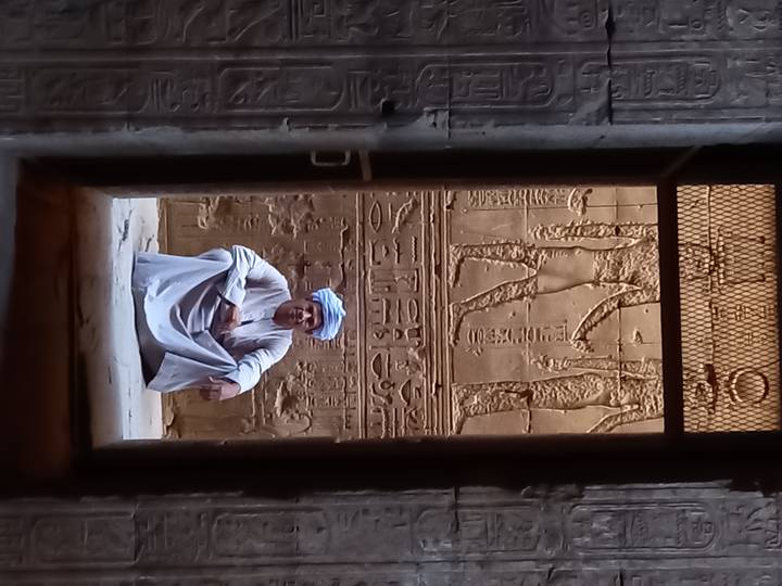 Personne assise devant des sculptures égyptiennes sur un mur.