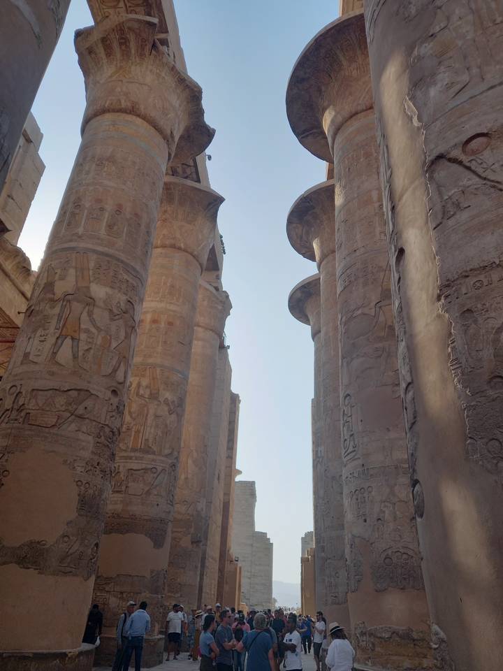 Groupe de personnes parmi des colonnes égyptiennes antiques avec des hiéroglyphes.