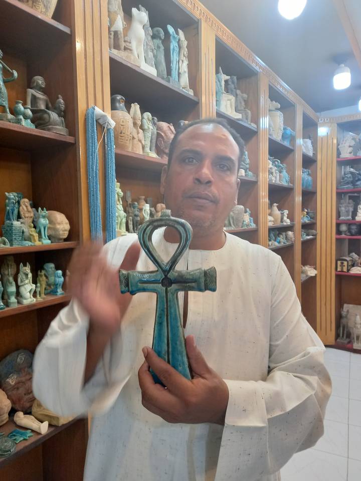 Personne tenant une grande croix égyptienne verte dans un magasin.