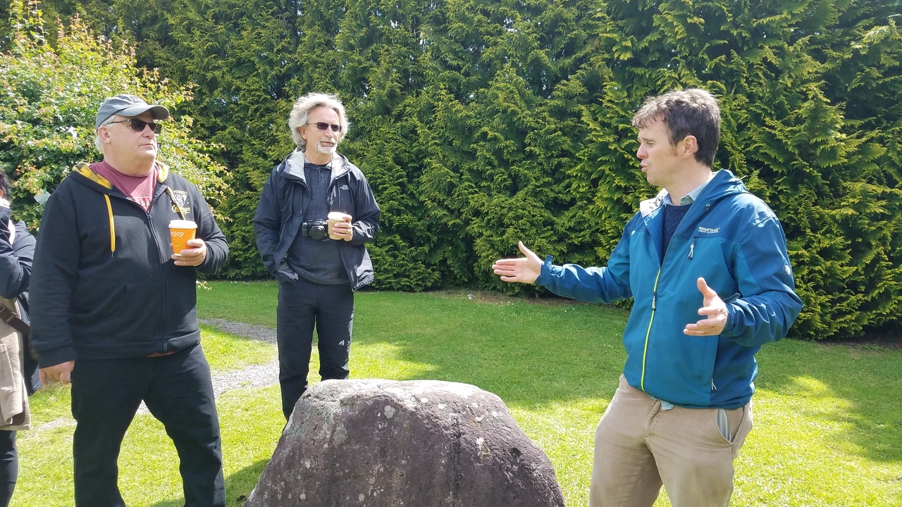 Groupe de touristes écoutant un guide à l'extérieur dans un jardin.