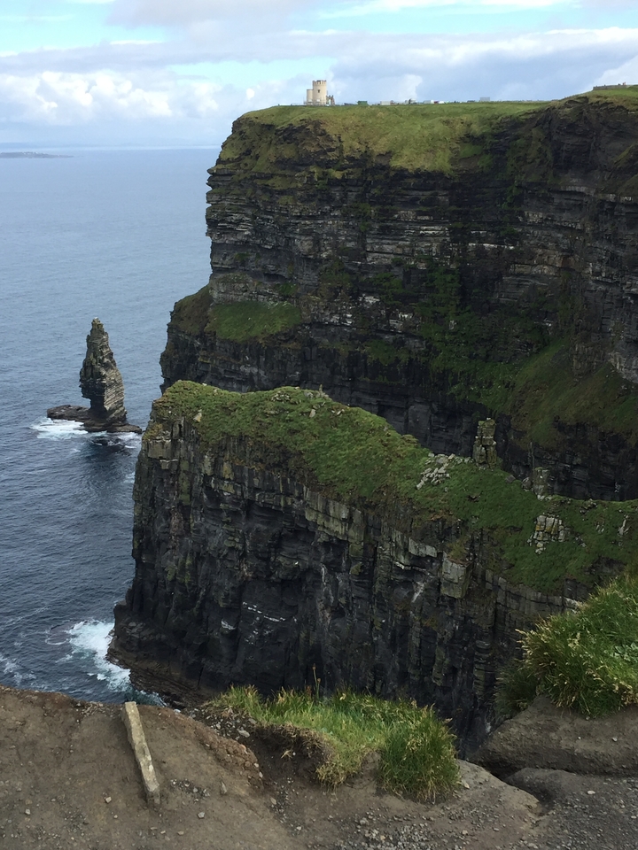 Cliffside with grassy top and rock formations meeting the ocean.