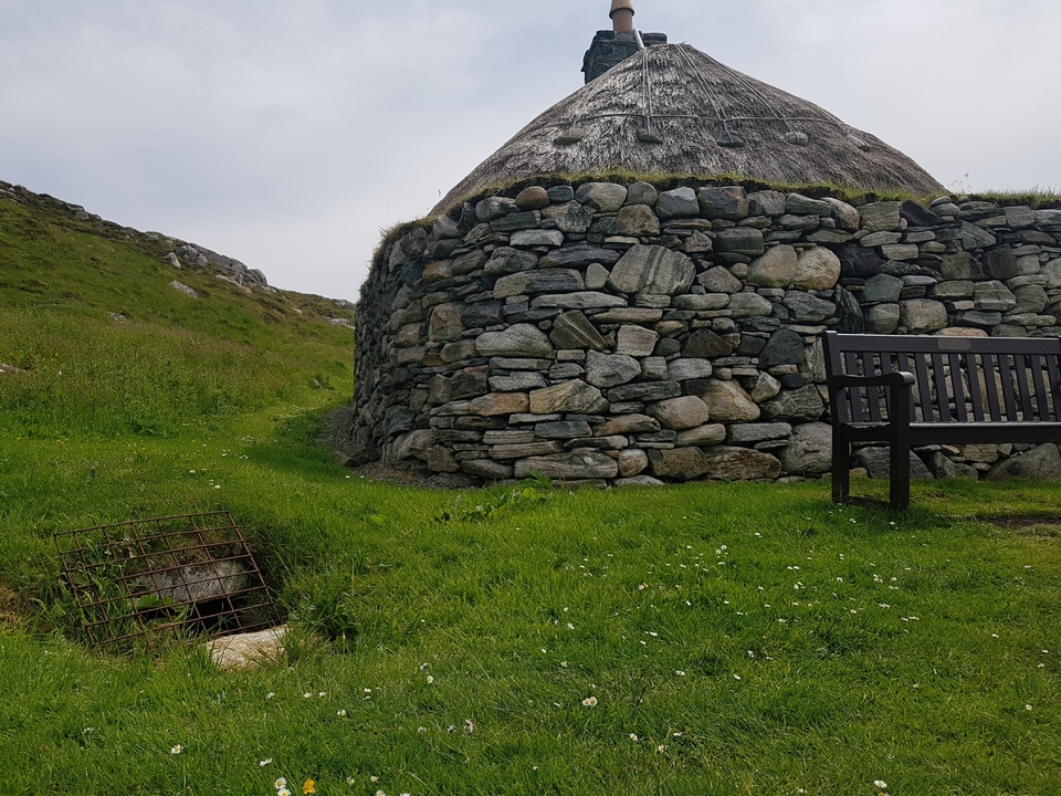 Structure circulaire en pierre sur une colline herbeuse.