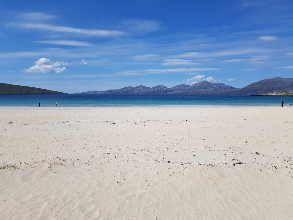 Large plage de sable avec une eau turquoise et des montagnes au loin.