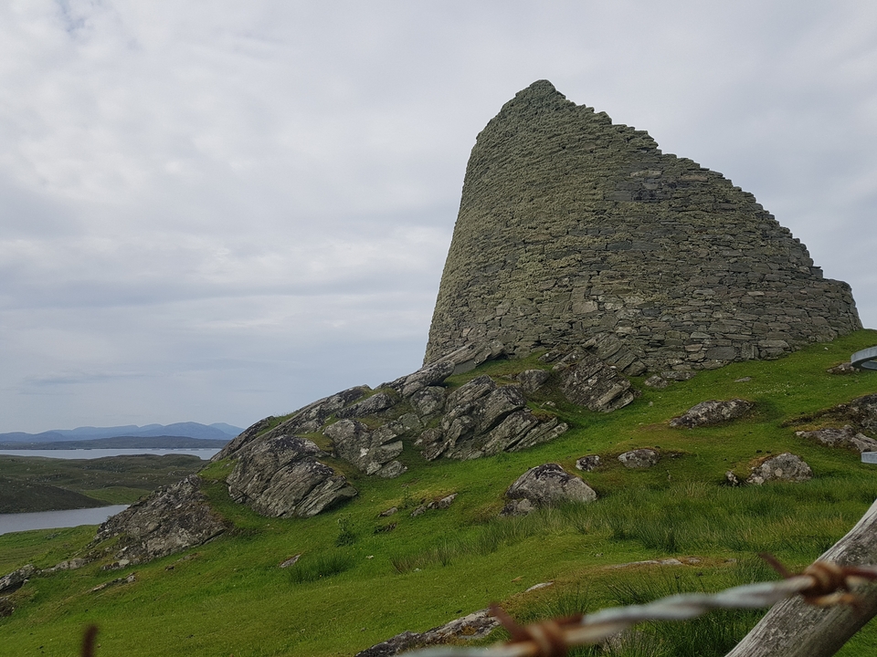 Structure en pierre sur une colline herbeuse avec des vues panoramiques alentour.