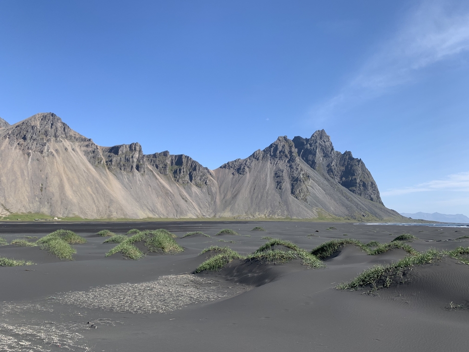 Black sand beach with grass-topped dunes and rugged mountains in the background.