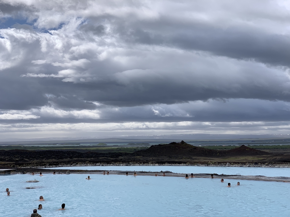 People relaxing in a geothermal pool with a cloudy sky above.