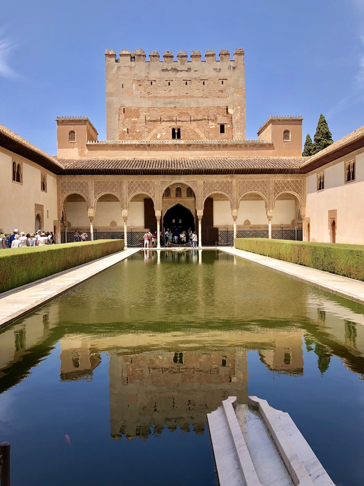 Cour historique avec un bassin et des arches, visitée par des touristes.