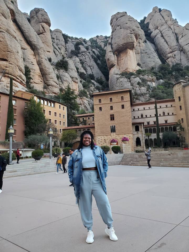 Personne qui pose devant un bâtiment historique avec un paysage montagneux en arrière-plan.