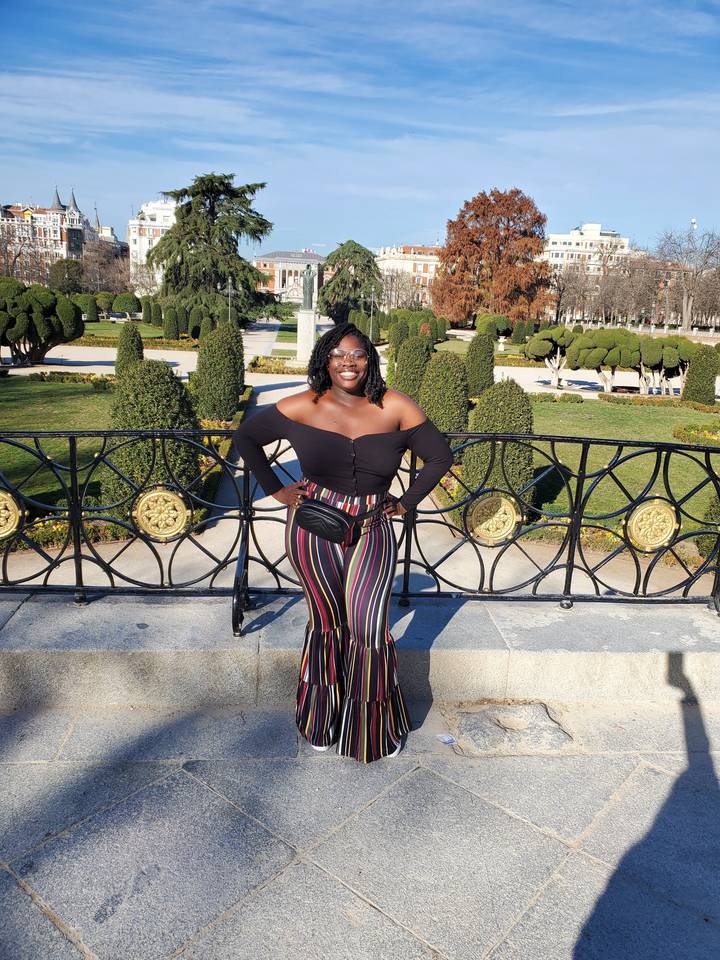 Personne qui pose dans un jardin avec des buissons taillés et des éléments architecturaux.