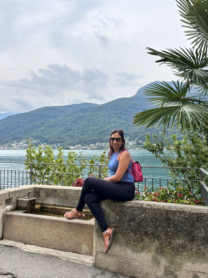 Femme assise sur un rebord avec un lac et des montagnes en arrière-plan.