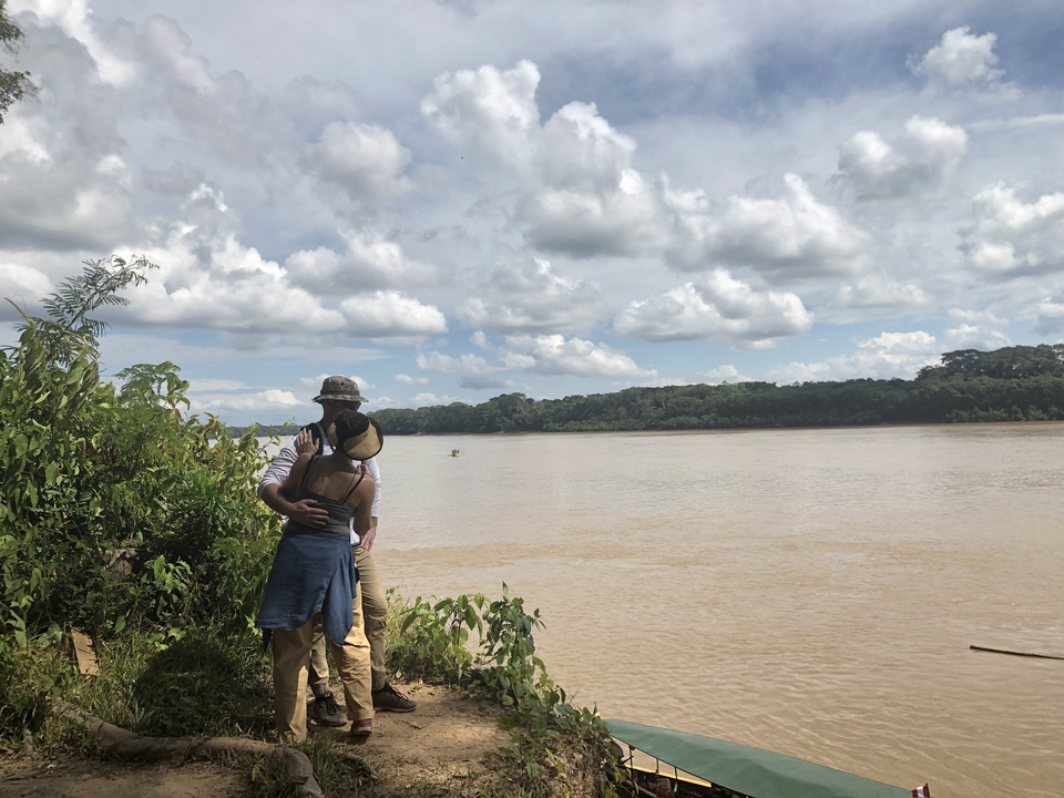Couple s'embrassant au bord d'une large rivière sous un ciel nuageux