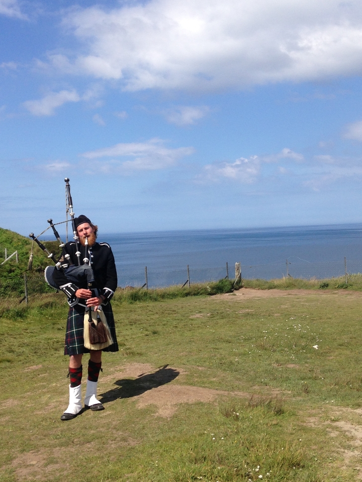 Homme en tenue traditionnelle écossaise jouant de la cornemuse au bord de la mer.