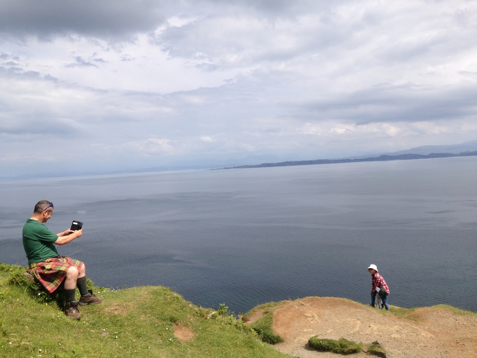 Un homme prenant une photo près d'une falaise surplombant une grande étendue d'eau.