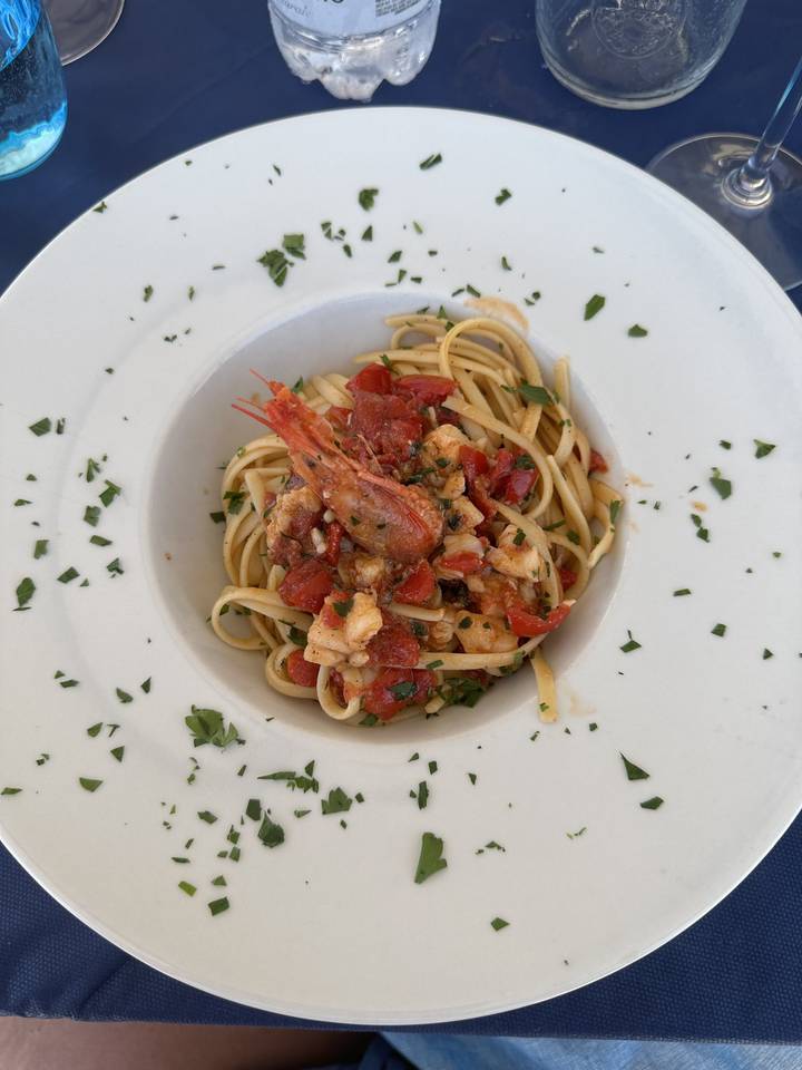 Assiette de pâtes aux crevettes et sauce tomate garnie d'herbes.