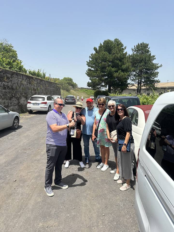 Groupe de personnes debout dans une zone de stationnement avec des arbres et des voitures.