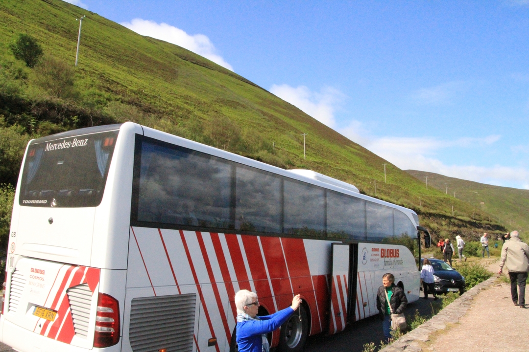 Des gens debout près d'un bus touristique dans un paysage vallonné.