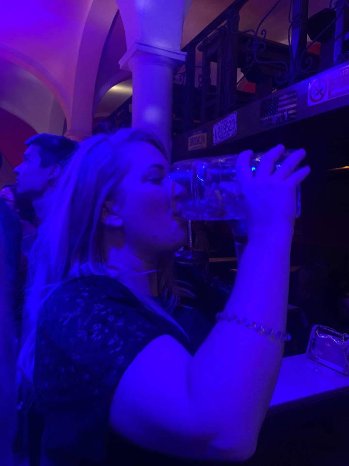Woman drinking from a large glass in low lighting.