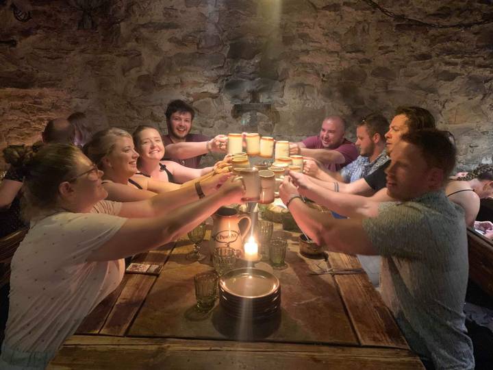 Group toasting with mugs in a stone-walled room.