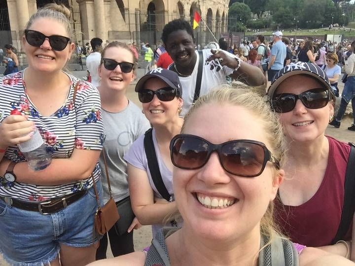 Group selfie of smiling tourists with a vendor in the background.